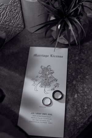 Black and white photograph of a marriage license document with two wedding rings placed on top.