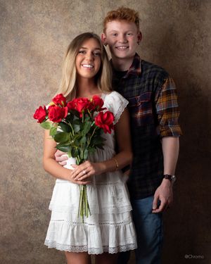 Couple poses with red roses against textured brown backdrop.