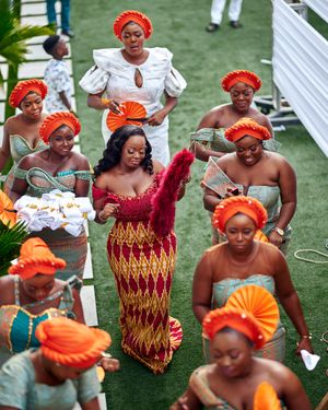 Traditional African wedding celebration with women in orange headwraps and colorful attire dancing.