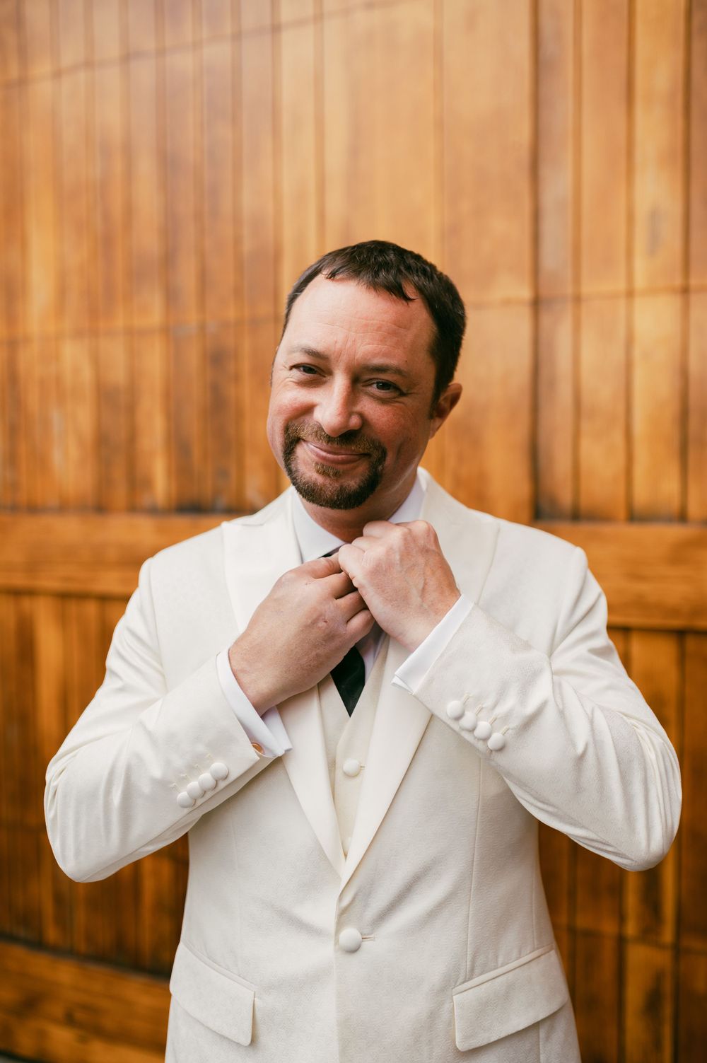 Person in a crisp white suit jacket against a wooden paneled wall.