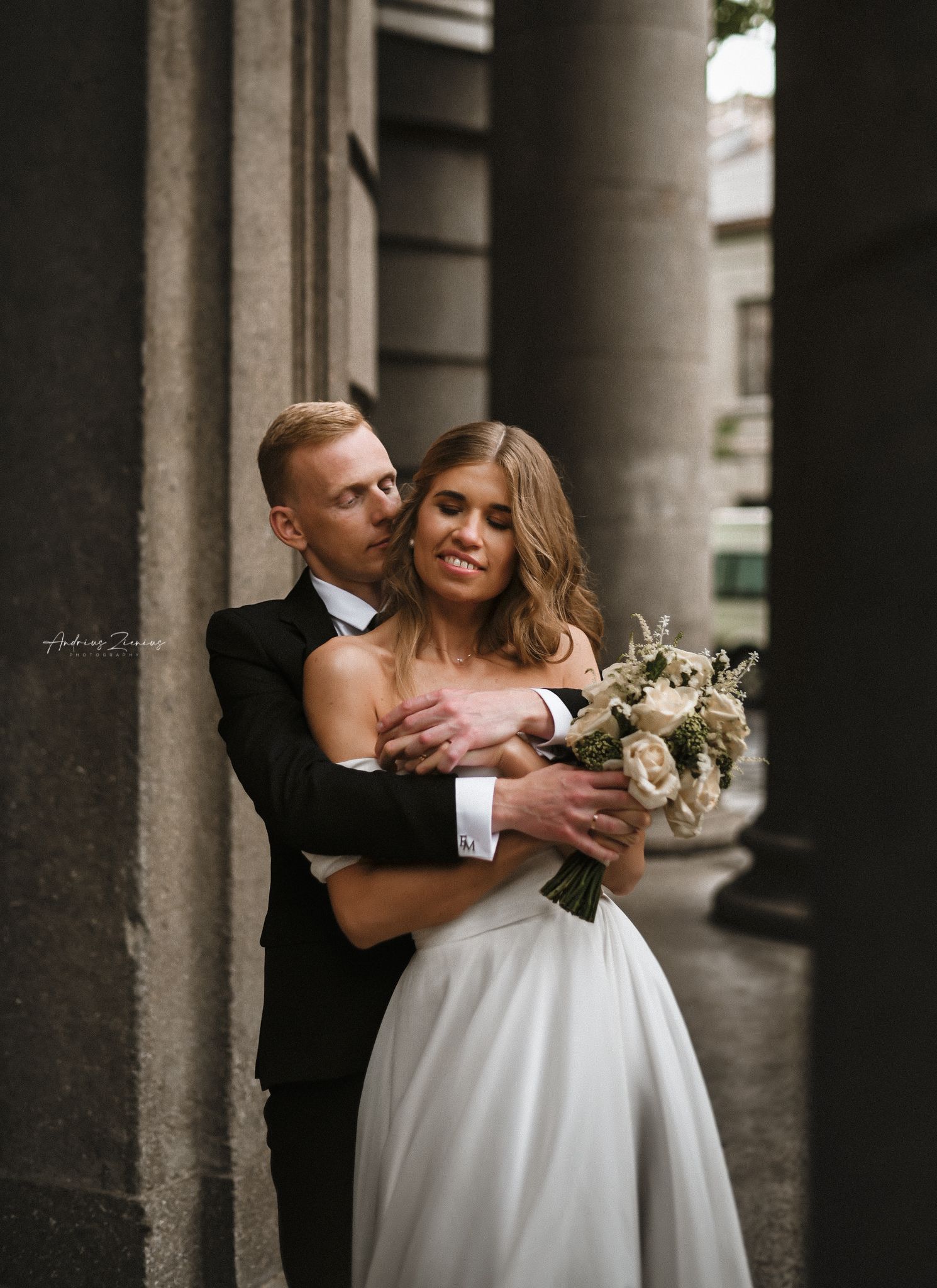 Romantic couple portrait in formal wear between elegant stone columns.