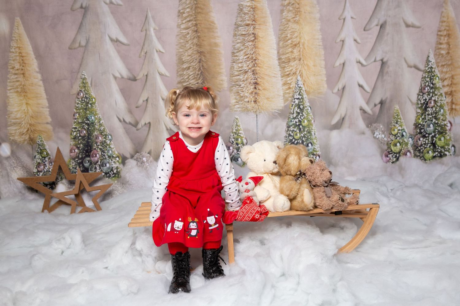 child in red dress sat on a sleigh in the snow with teddies