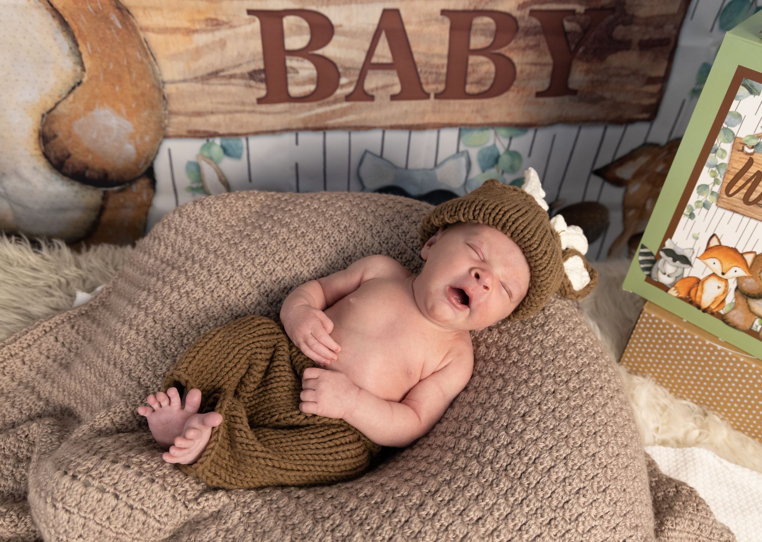 Newborn photography setup with rustic wooden baby sign and neutral tones.