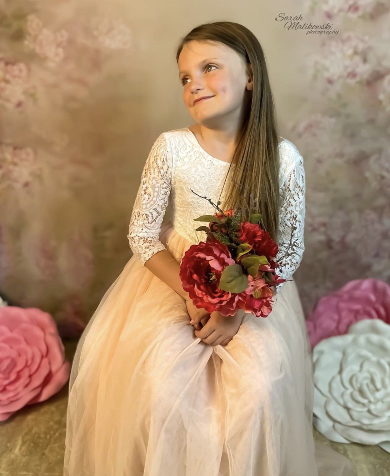 A romantic portrait with a peach tulle dress holding red roses against a soft background.