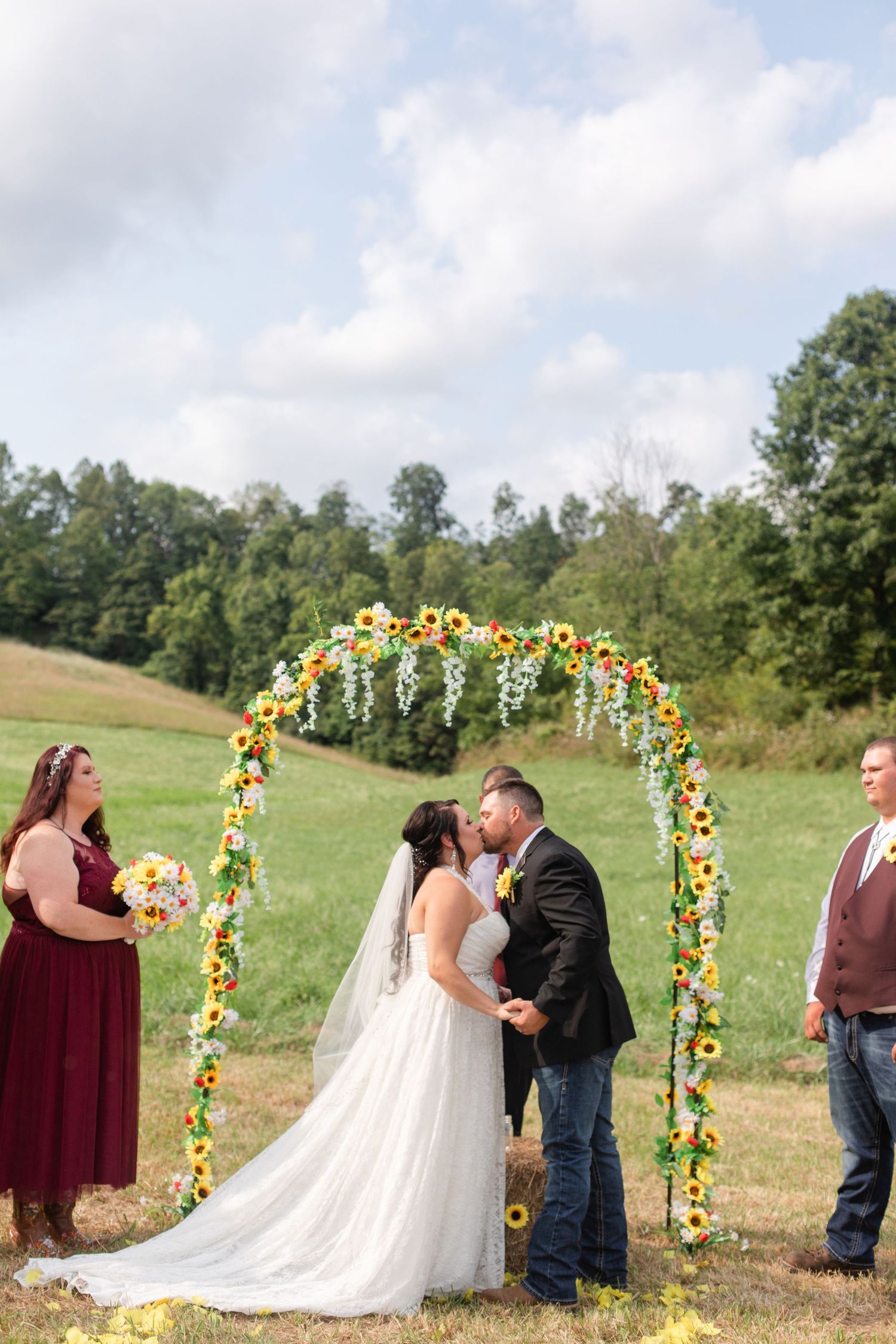 Outdoor wedding ceremony under sunflower arch with burgundy and white color scheme.