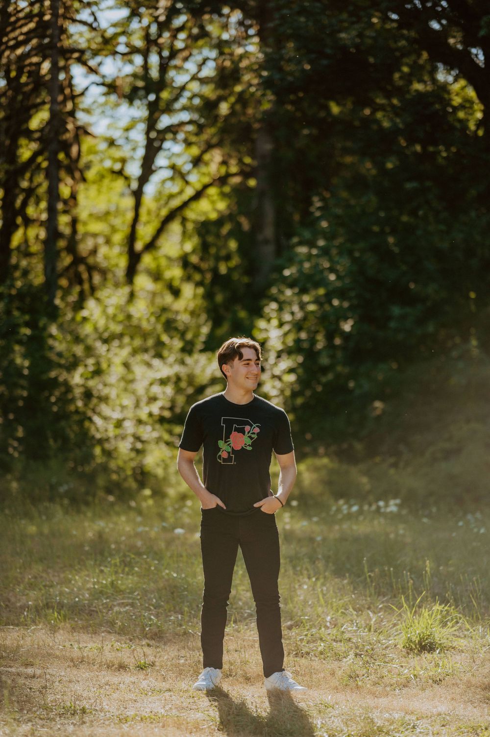 Person in black t-shirt standing in a sunlit meadow with trees in the background.