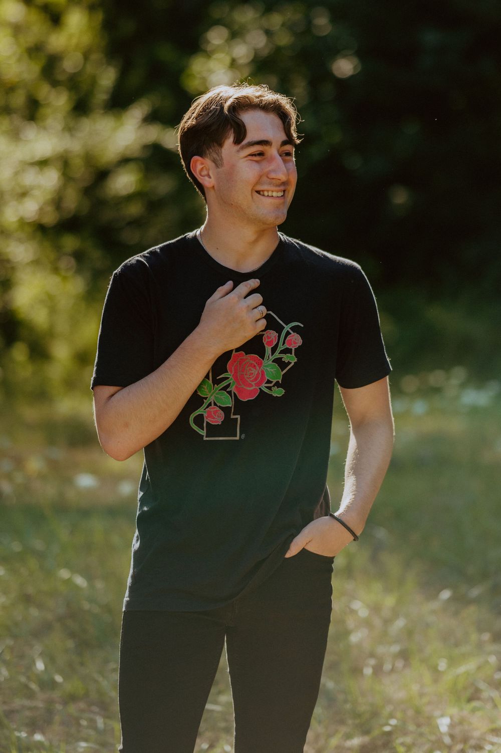 A person wearing a black t-shirt with floral design stands in golden sunlight against a natural backdrop.