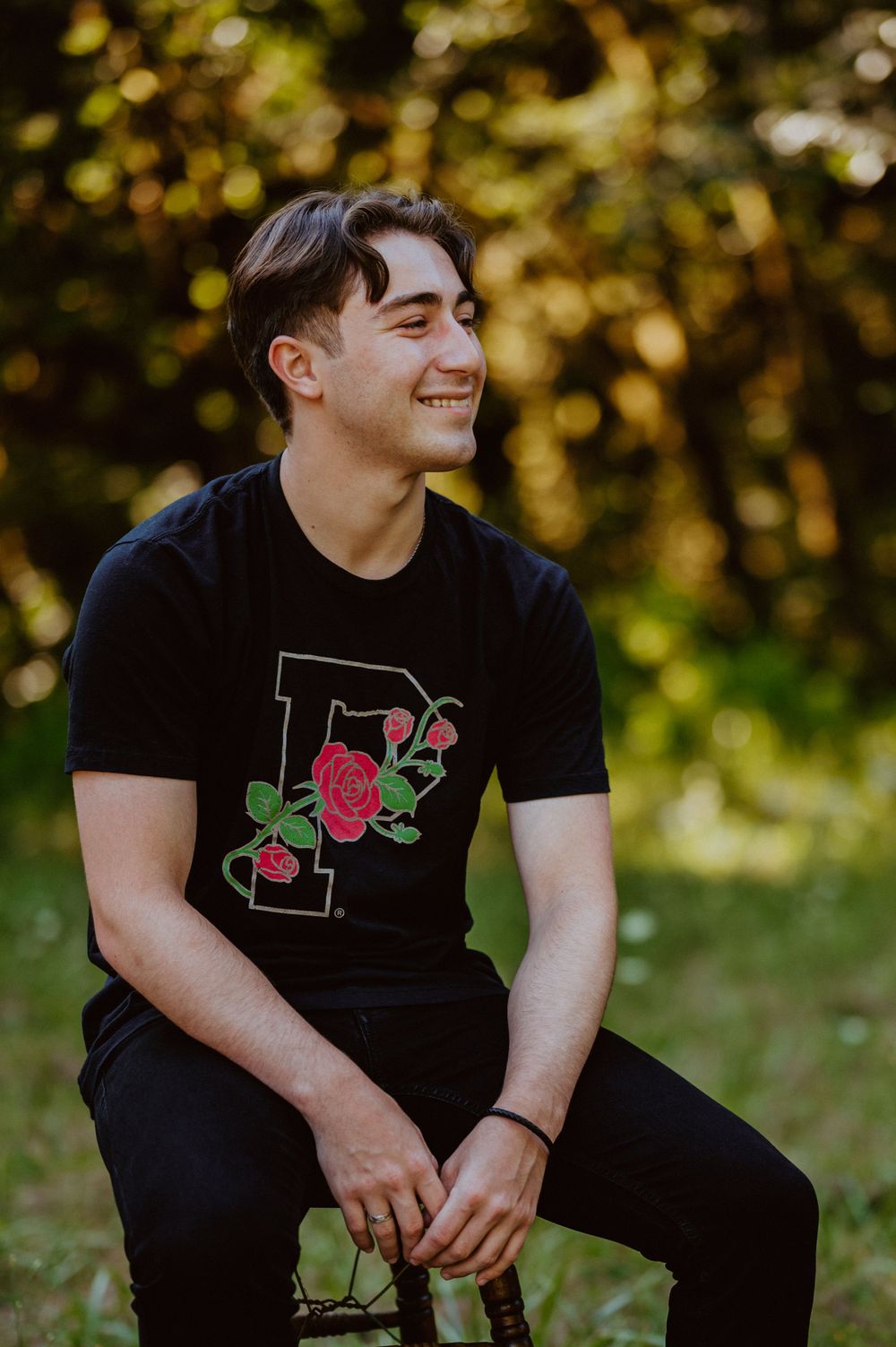 Person in black t-shirt with rose design sitting outdoors during golden hour.