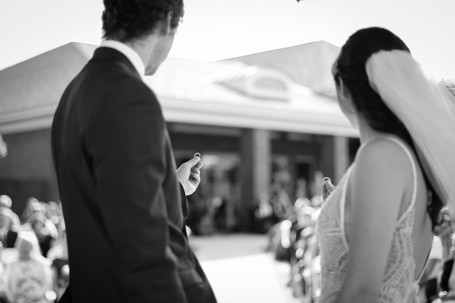 A black and white wedding ceremony photo showing a couple exchanging vows outdoors.