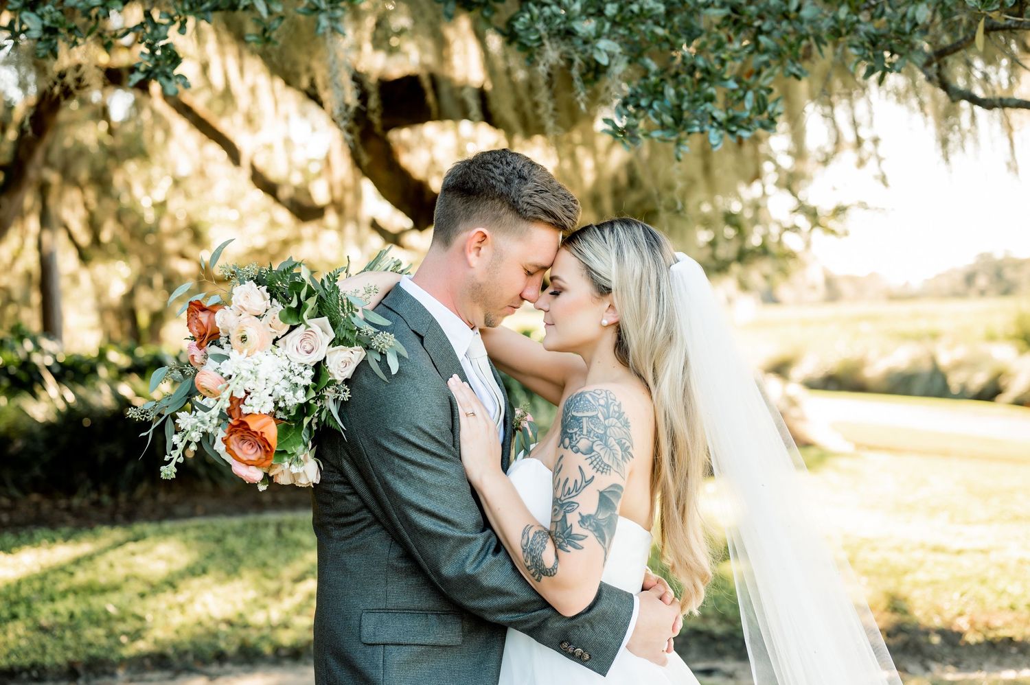 Couple shares romantic moment under Spanish moss trees during outdoor wedding portraits.