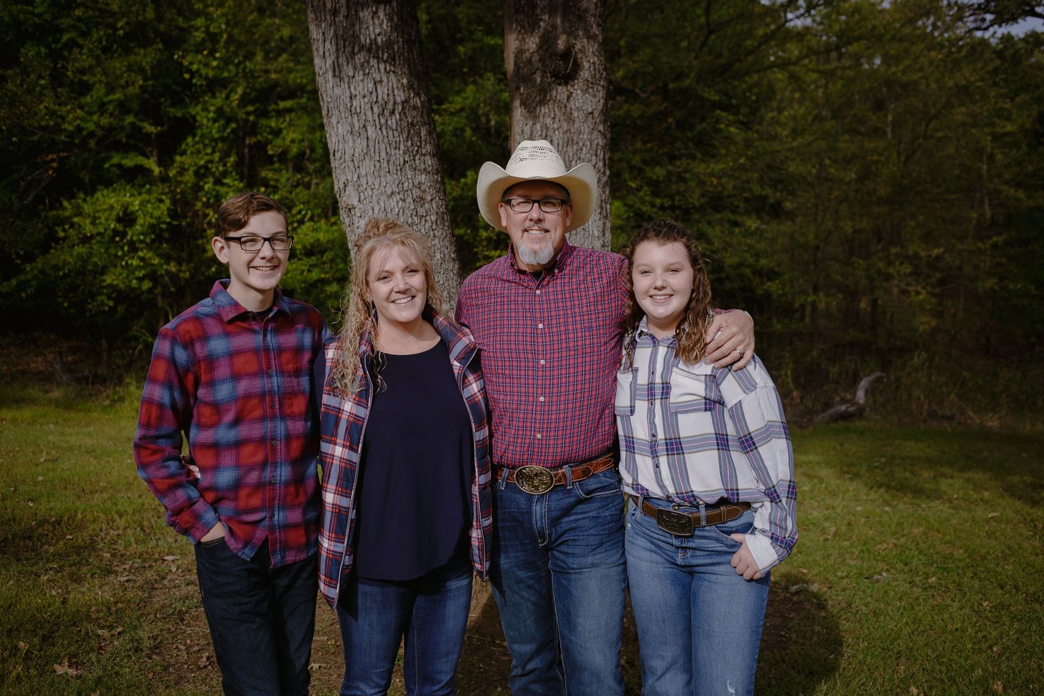 A casual outdoor family portrait with western attire standing in front of trees at Loy Lake Park, Denison, Texas