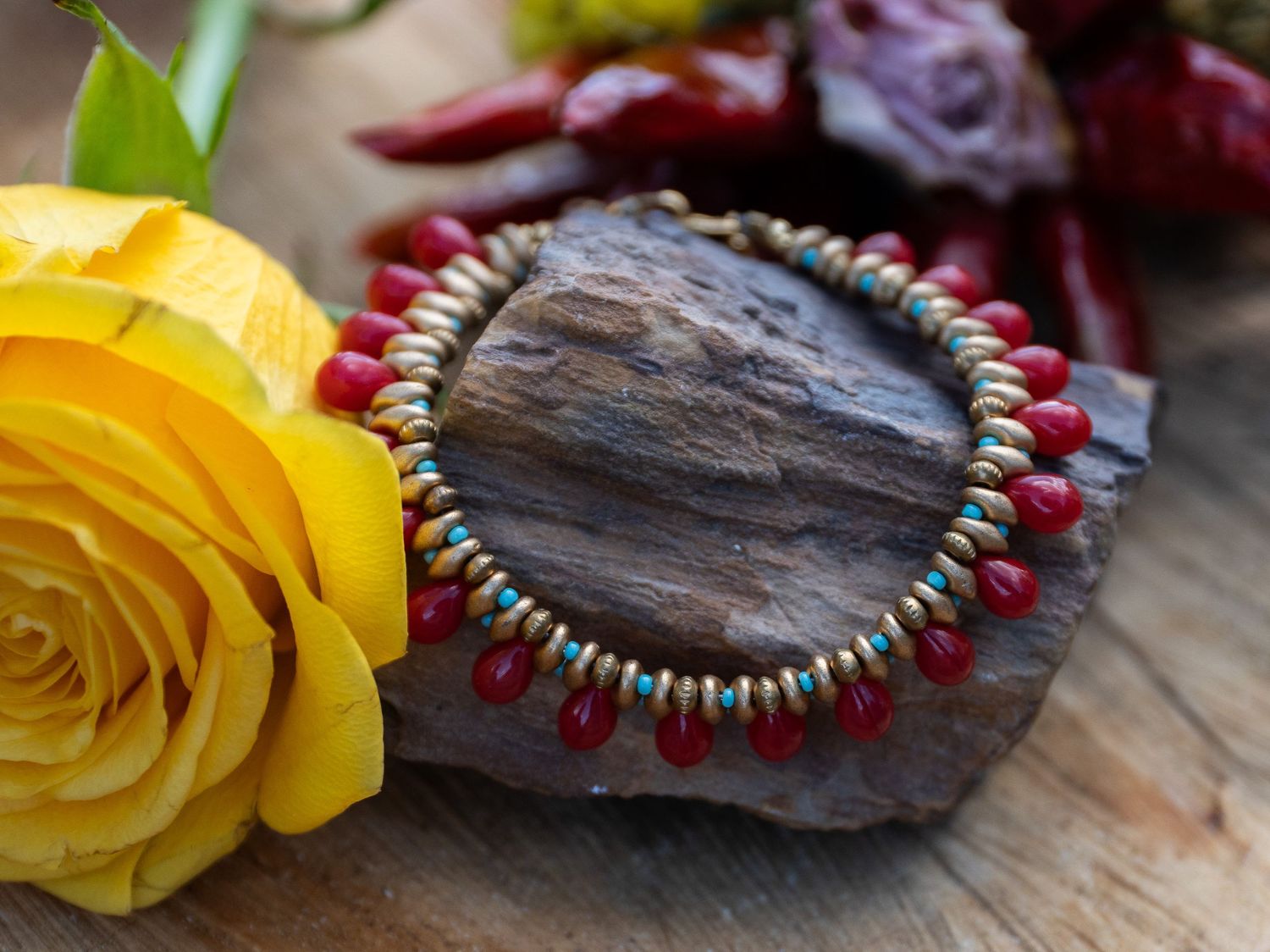 Colorful beaded jewelry and yellow rose displayed on rustic wooden surface.