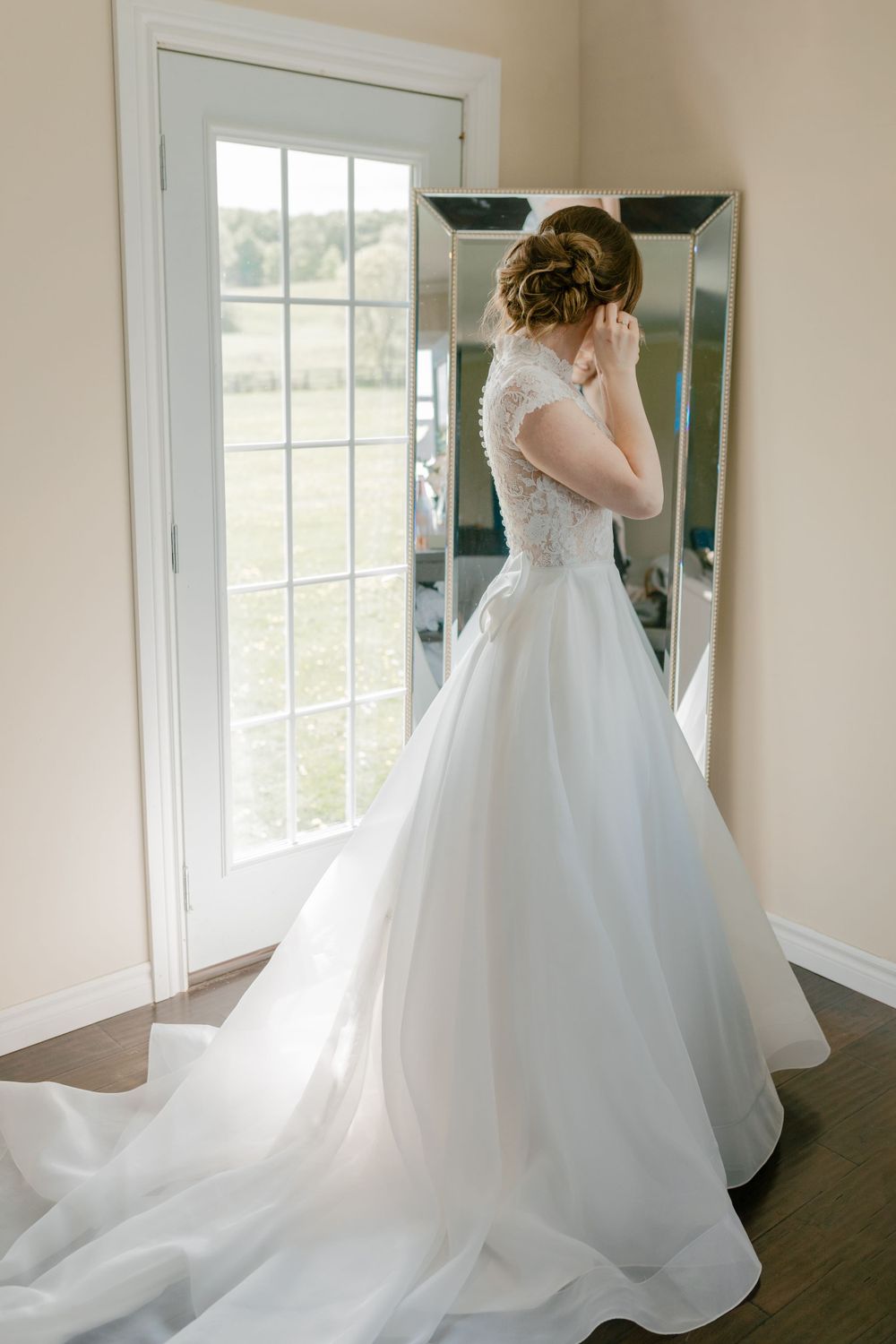 Wedding dress preparation sequence showing the flowing train and lace details in a bright room.
