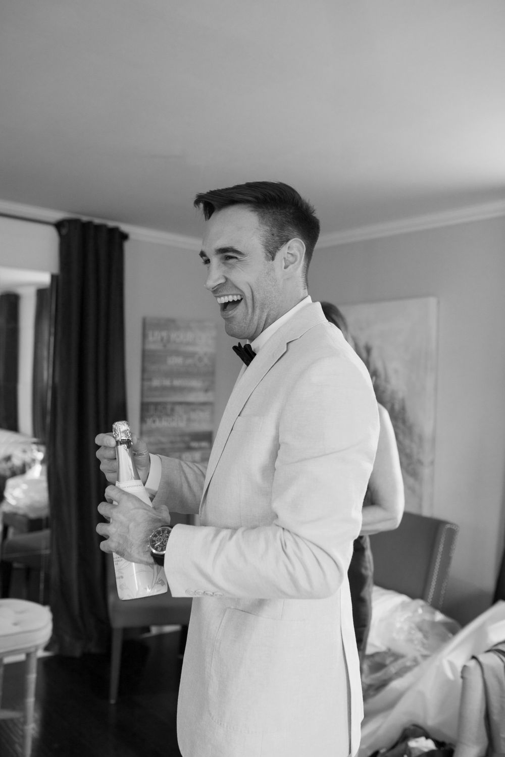 Black and white photo of person in white shirt laughing while getting ready in a room.