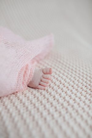Close-up of tiny baby foot wrapped in pink lace against textured blanket.