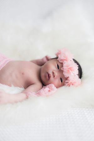 Sleeping baby with pink floral headband on white textured backdrop.