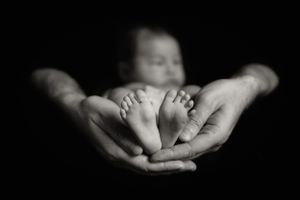 Black and white photo of tiny baby feet cradled in adult hands.