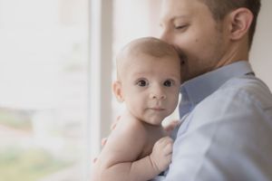 Tender family moments captured by window in soft natural light.