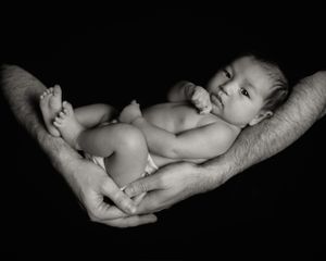 Black and white portrait of newborn resting in protective adult hands.
