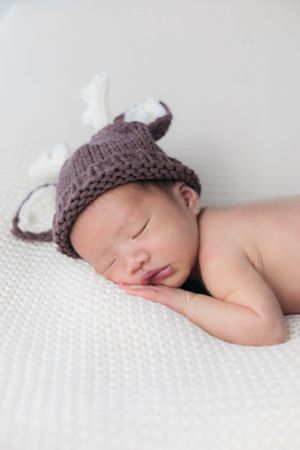 Sleeping newborn wearing knit animal hat on white textured blanket.