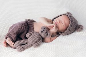 Newborn baby sleeping in cozy brown knitted outfit on white background.