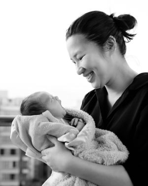 Tender moment between mother and newborn baby captured in black and white outdoor portrait.