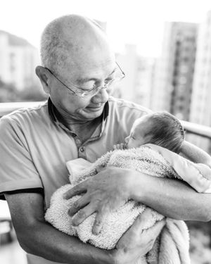 Black and white portrait of tender moment between grandfather and newborn on balcony.