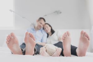 Bare feet of a couple relaxing on a white bed with their baby between them.