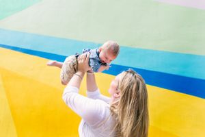Woman lifting baby high in air against colorful striped background.