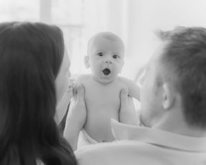 Baby being lifted up by parents against bright window background.