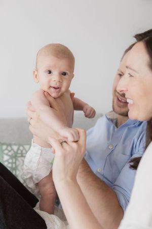 Happy baby in diaper being held up while on couch.
