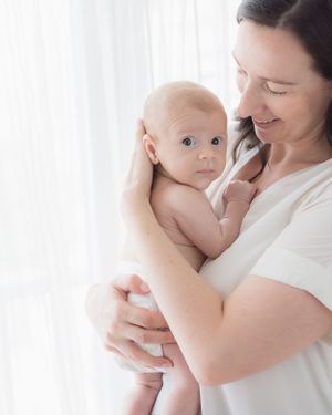 Tender moment between baby and mother against white curtain background.