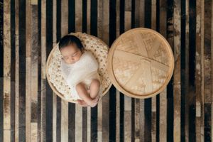 Overhead view of sleeping newborn in white outfit next to wooden circular decor.