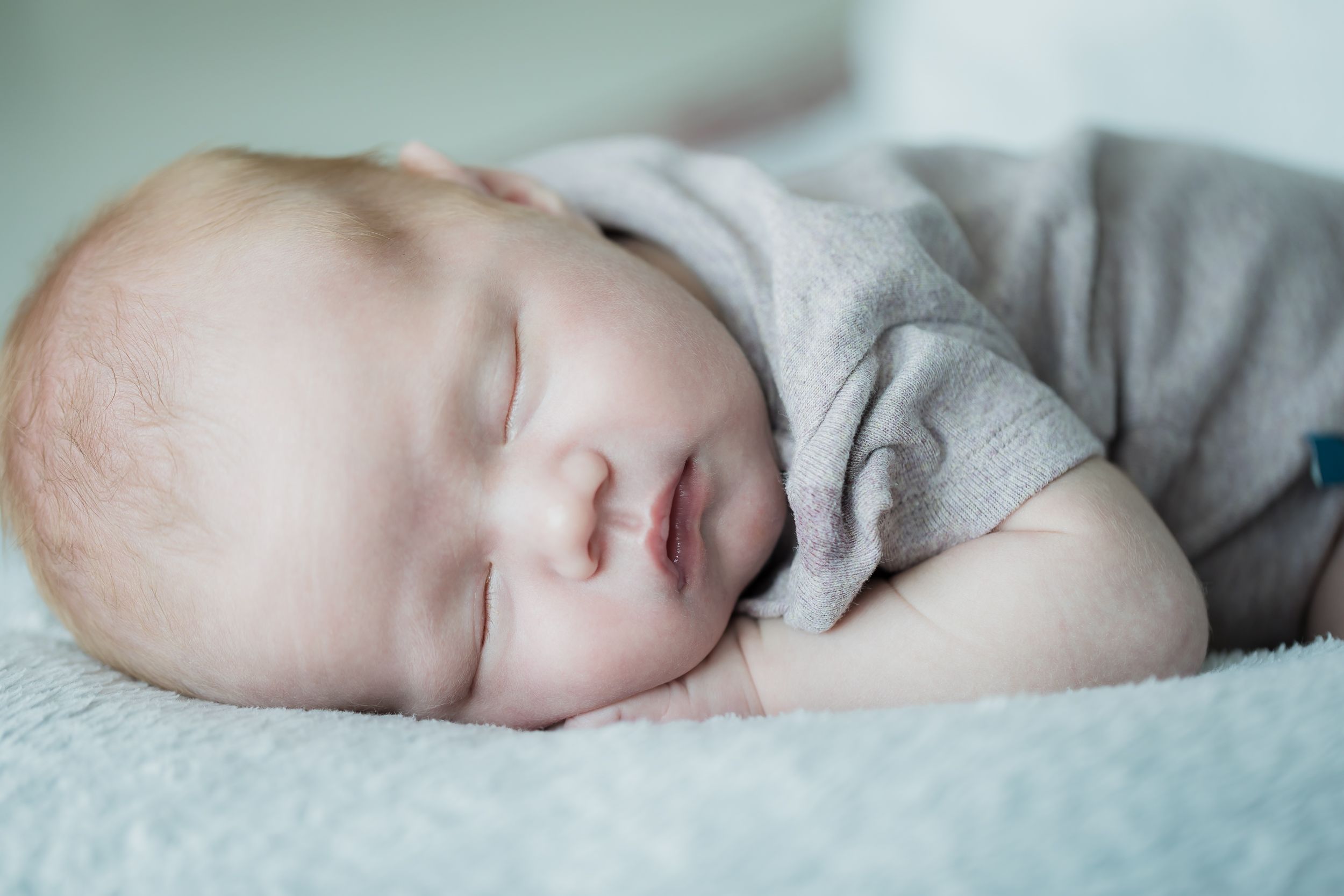 Peaceful sleeping baby in grey outfit resting on light blue blanket.