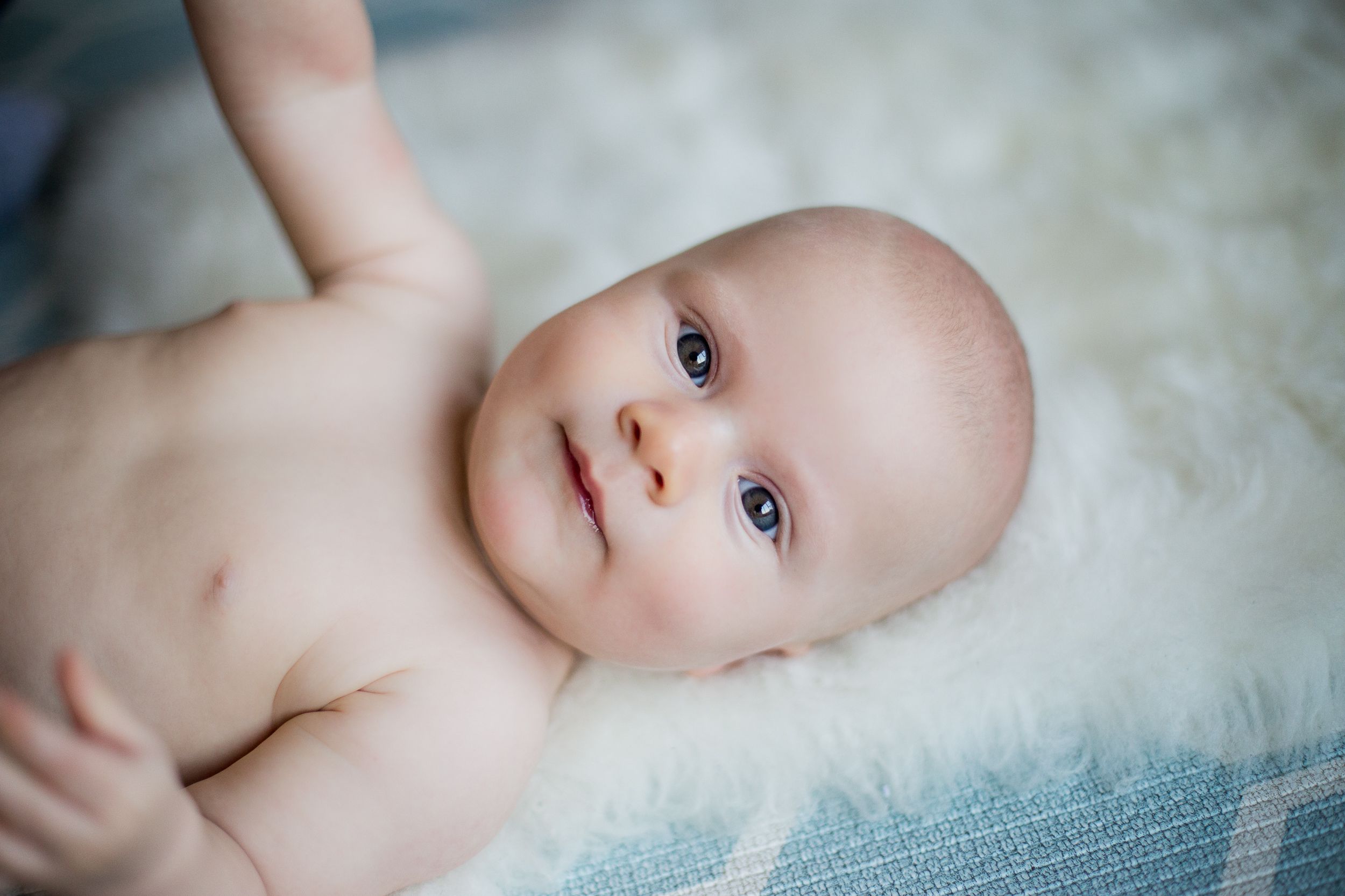 Baby lying on soft white blanket looking up with bright blue eyes.