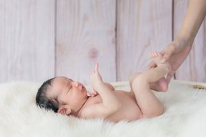 Newborn baby stretching during gentle massage on soft white surface.