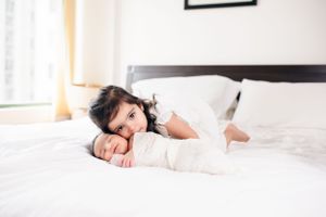 Sweet moment captured of family snuggling together on white bed in sunlit room.