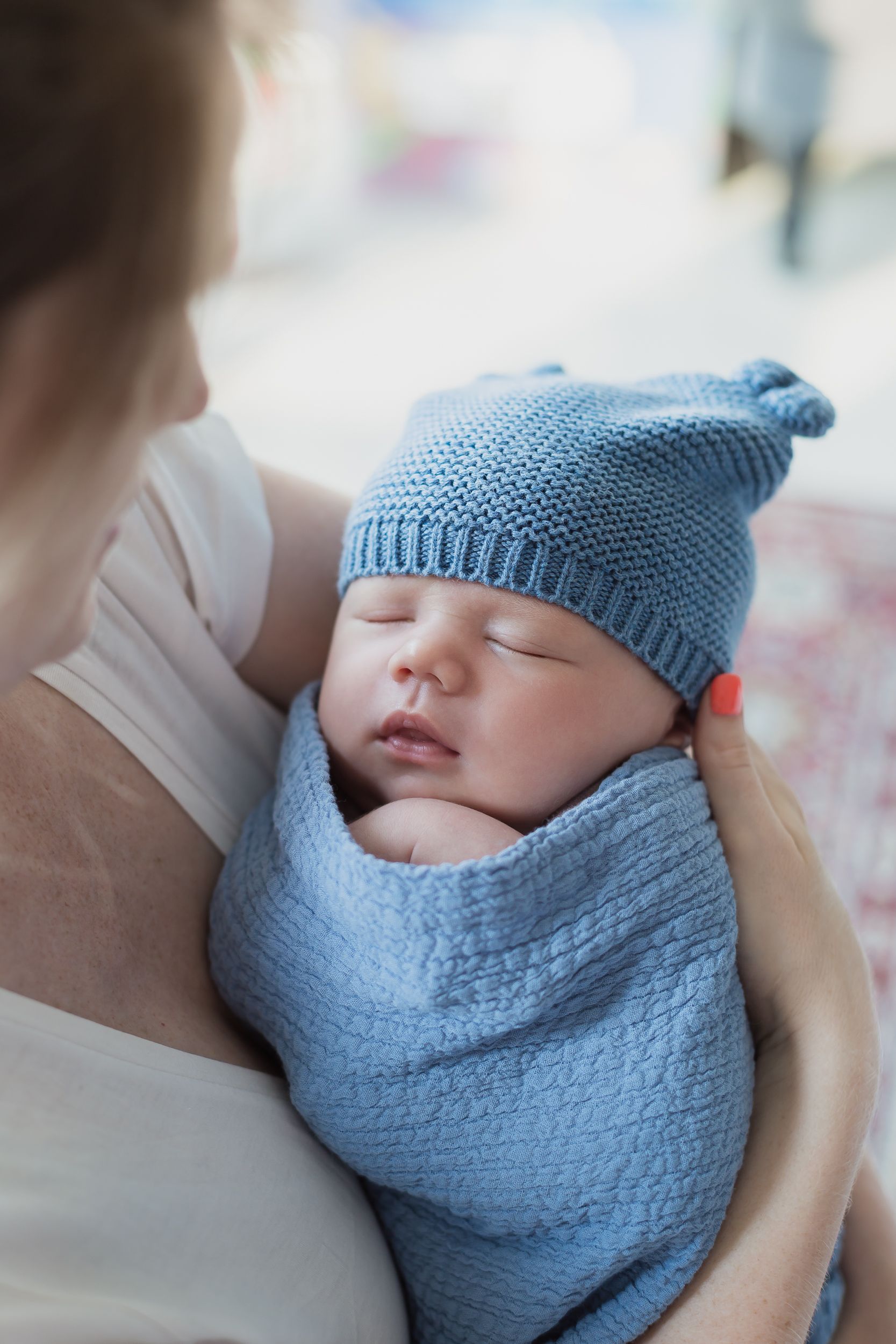 Newborn baby wearing blue knit hat sleeping while being cradled.