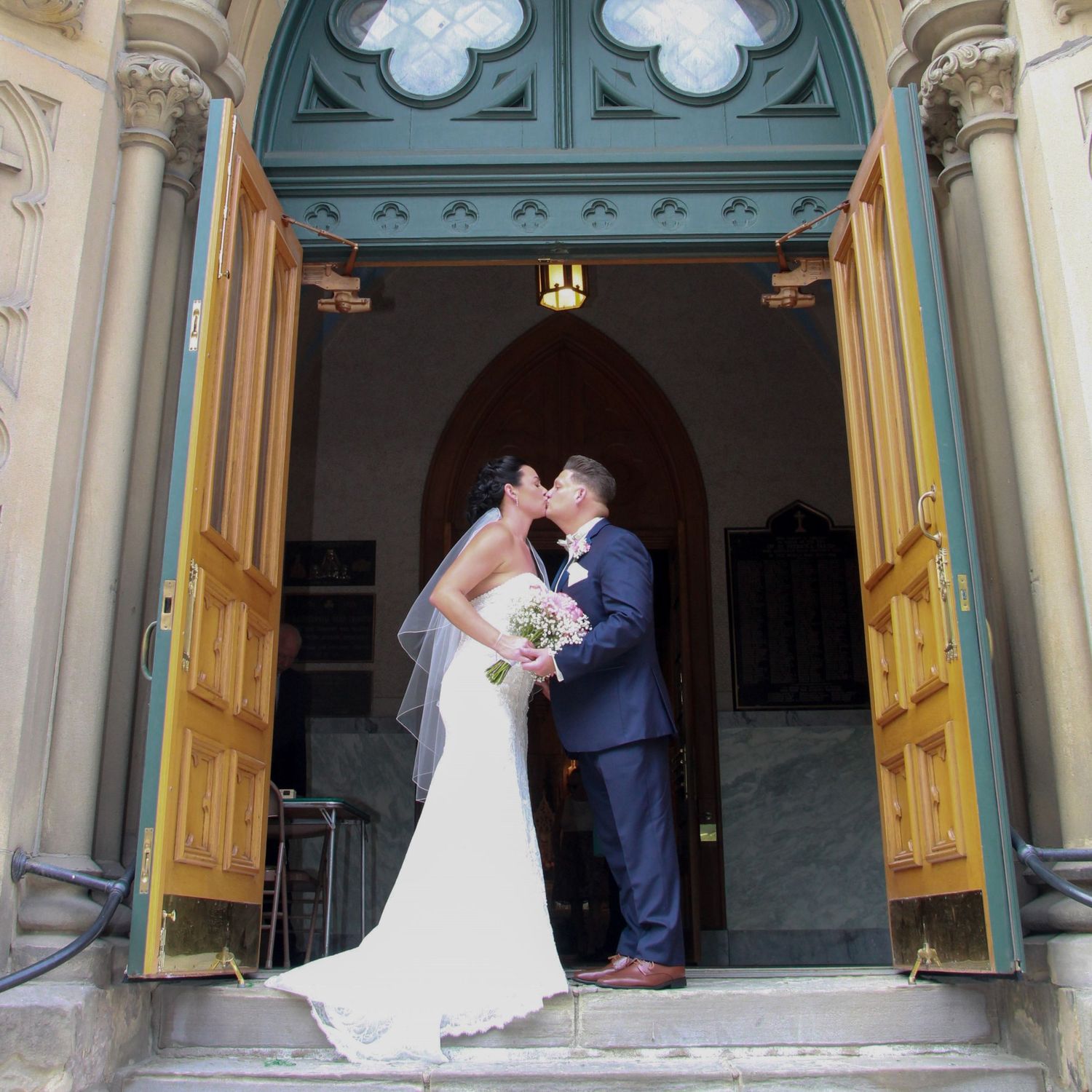 A couple shares their first kiss as newlyweds in front of ornate church doors.