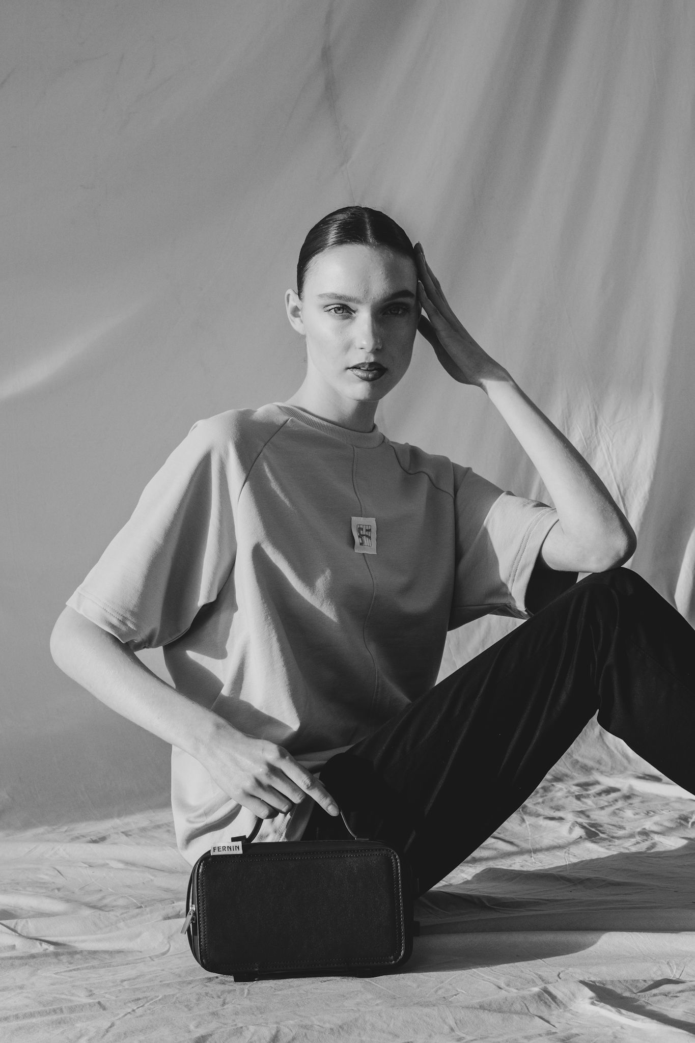 Zwart-wit portret van een model zittend op de vloer met een rustige, introspectieve houding in een studio setting.