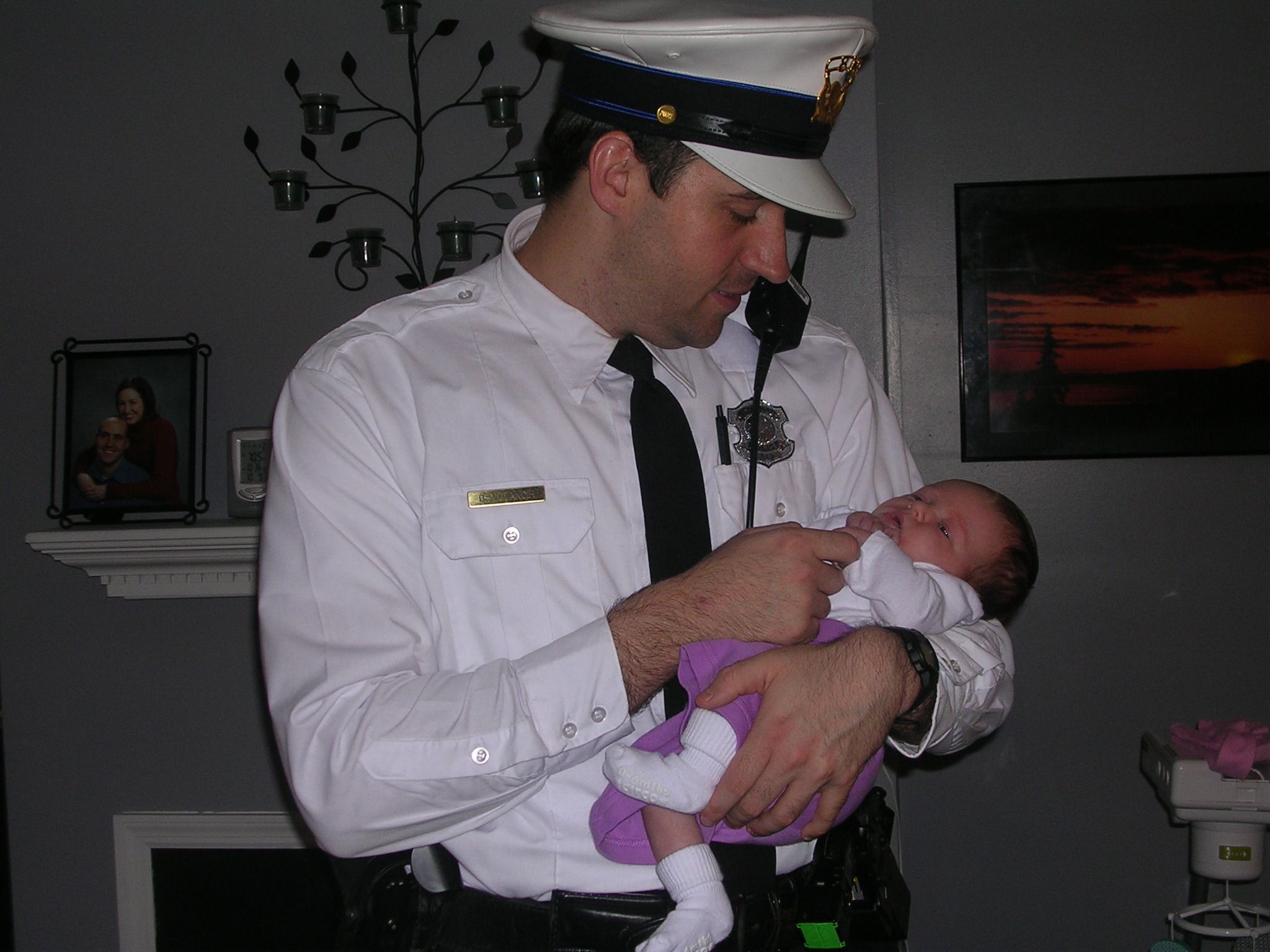A uniformed officer in white dress attire gently holds a swaddled infant.