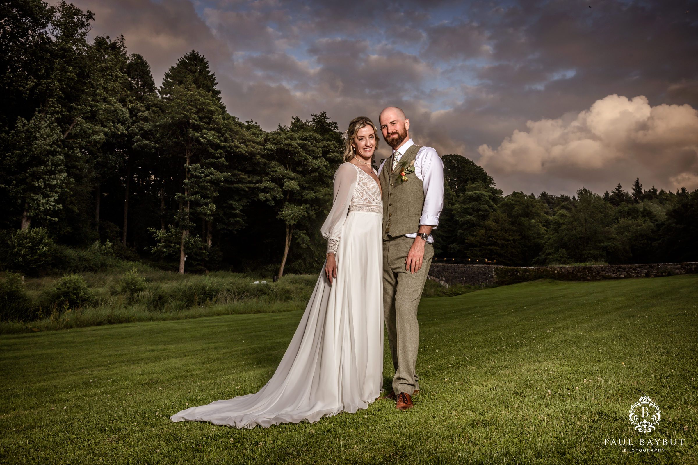 Wedding couple posing at sunset on a grassy hill with forest backdrop.