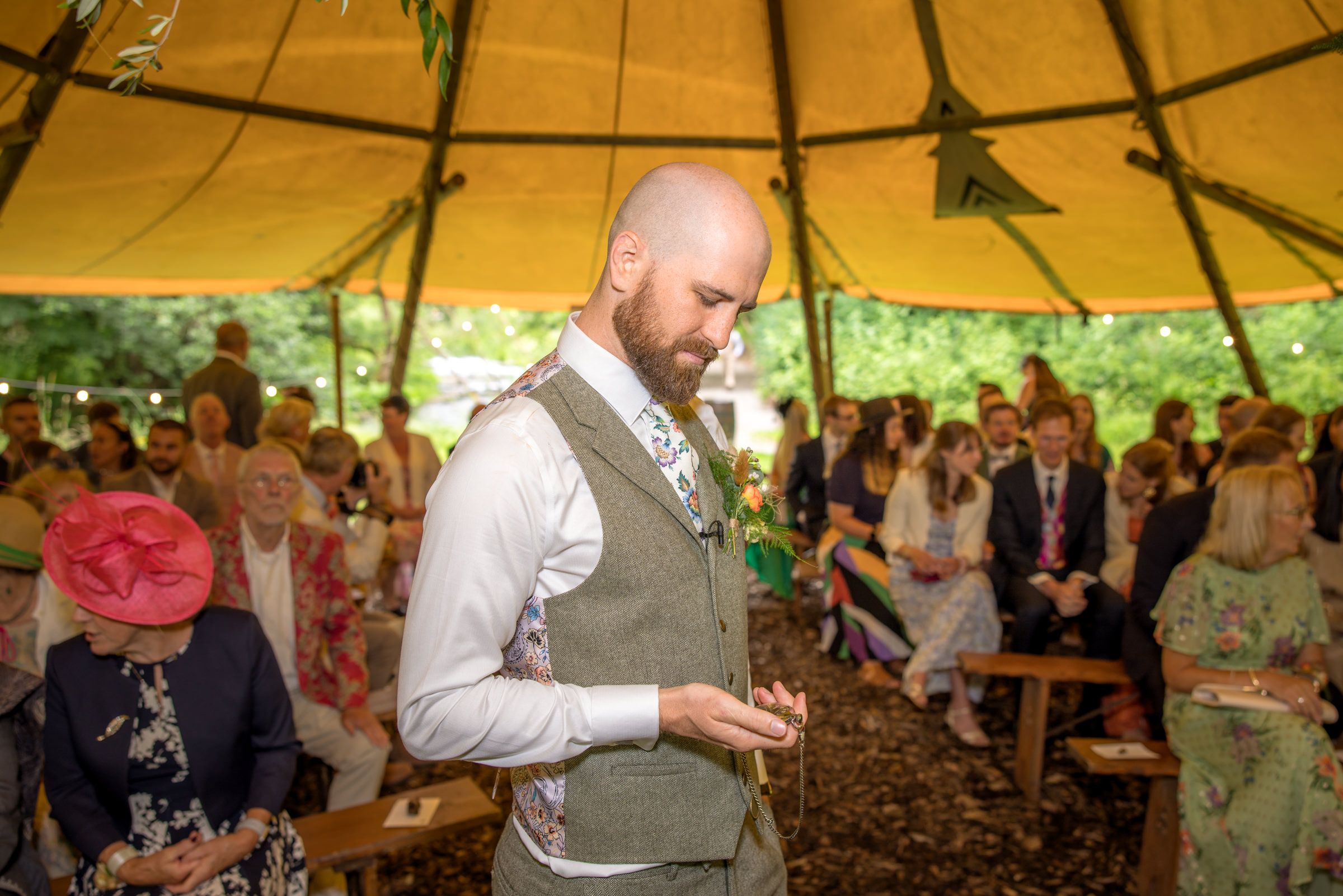 Wedding ceremony under a yellow canvas tent with guests seated on wooden benches.