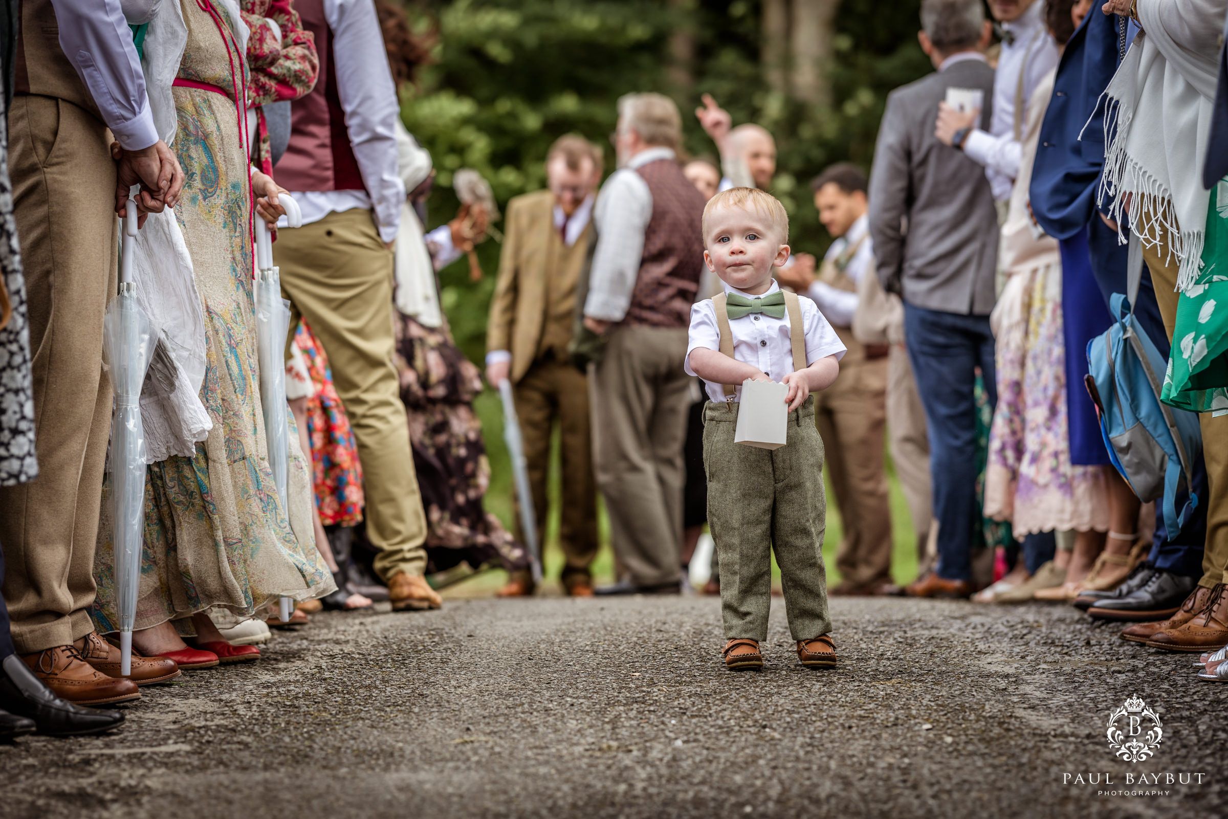 A small child walks down an aisle between rows of wedding guests outdoors.