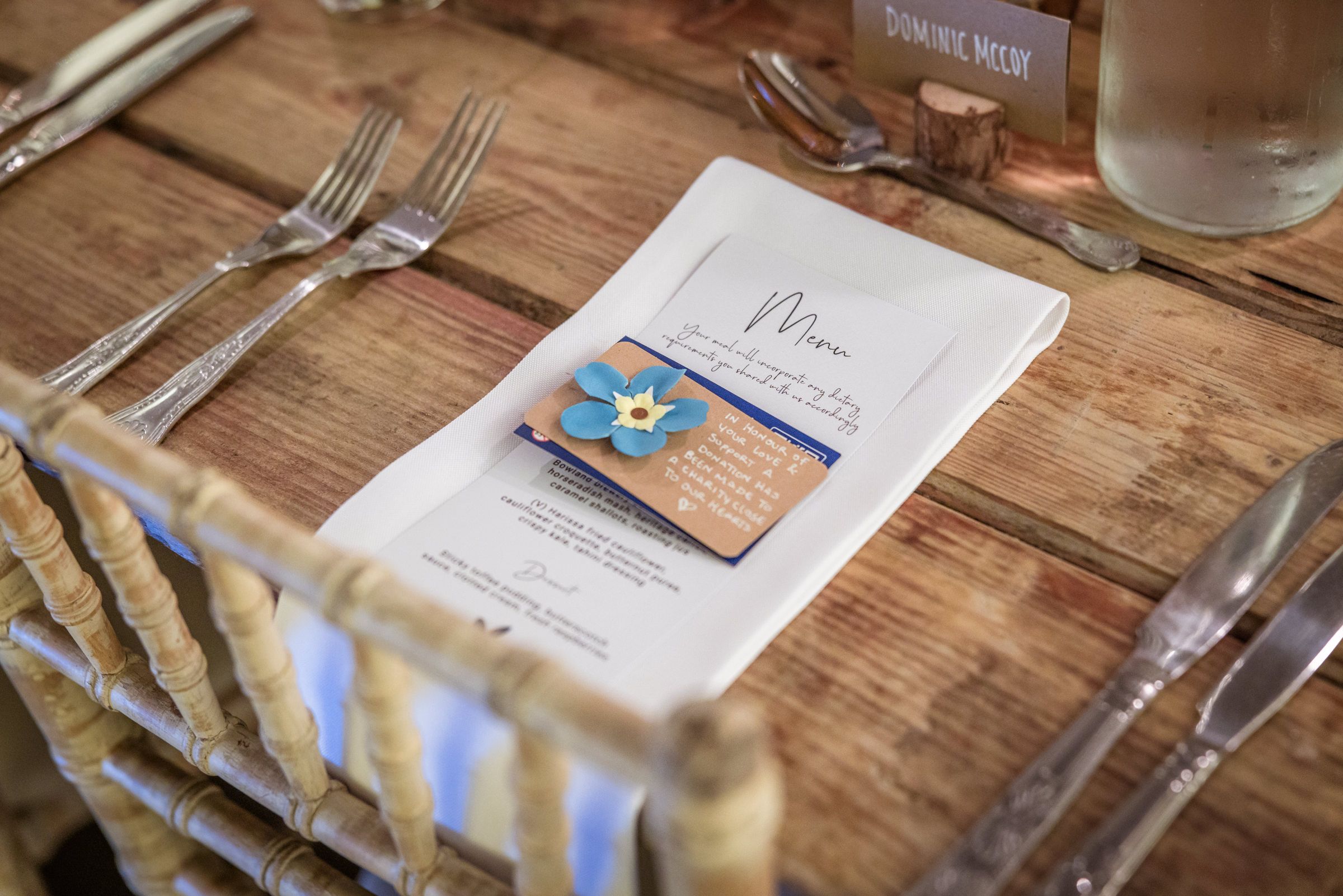 Wedding menu and place setting with blue flower detail on rustic wooden table.