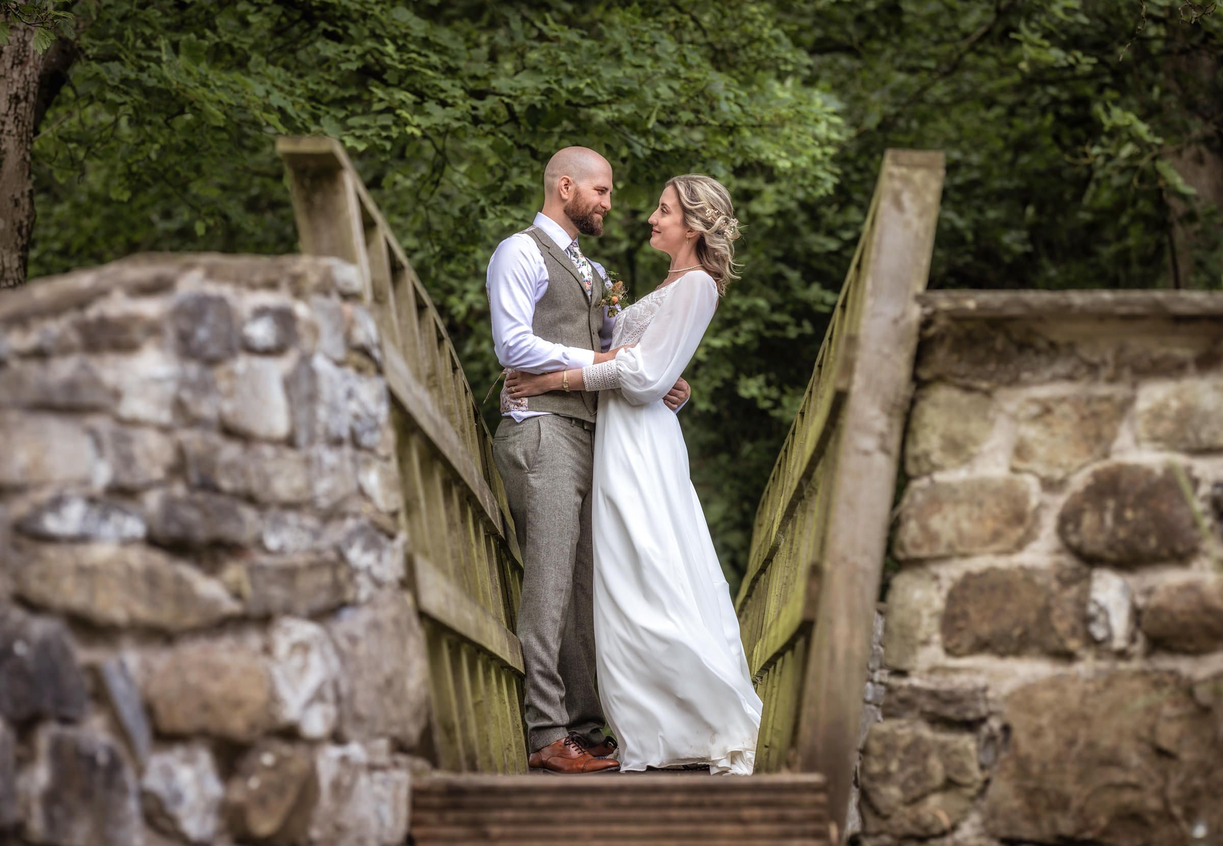 Wedding couple sharing intimate moment on rustic wooden bridge.