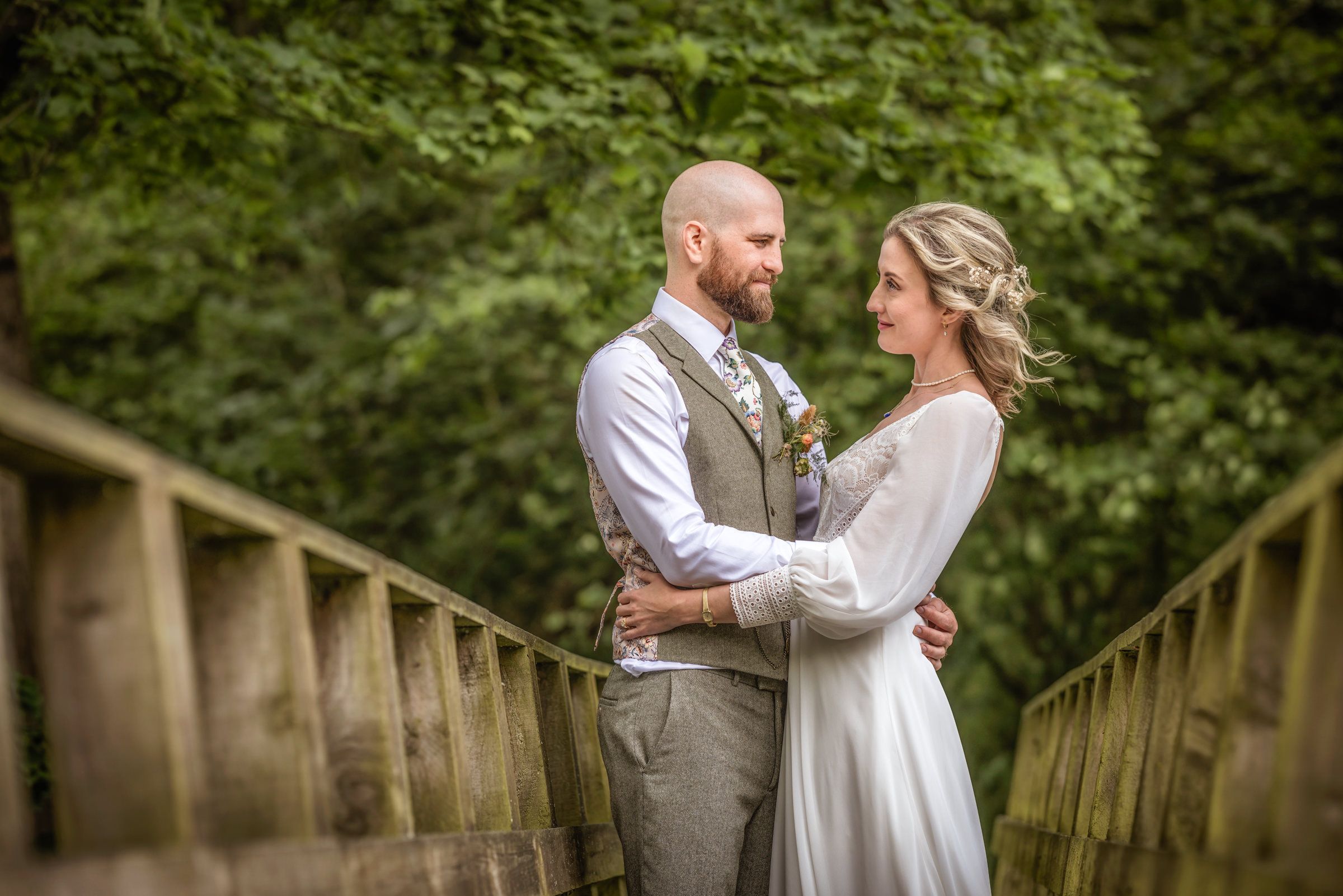 Romantic couple embracing on rustic wooden bridge during wedding photoshoot.