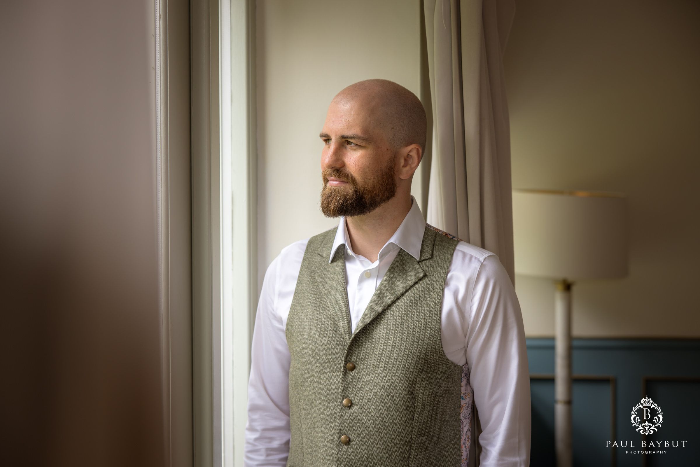Classic pre-wedding portrait by a window featuring formal attire and natural lighting.