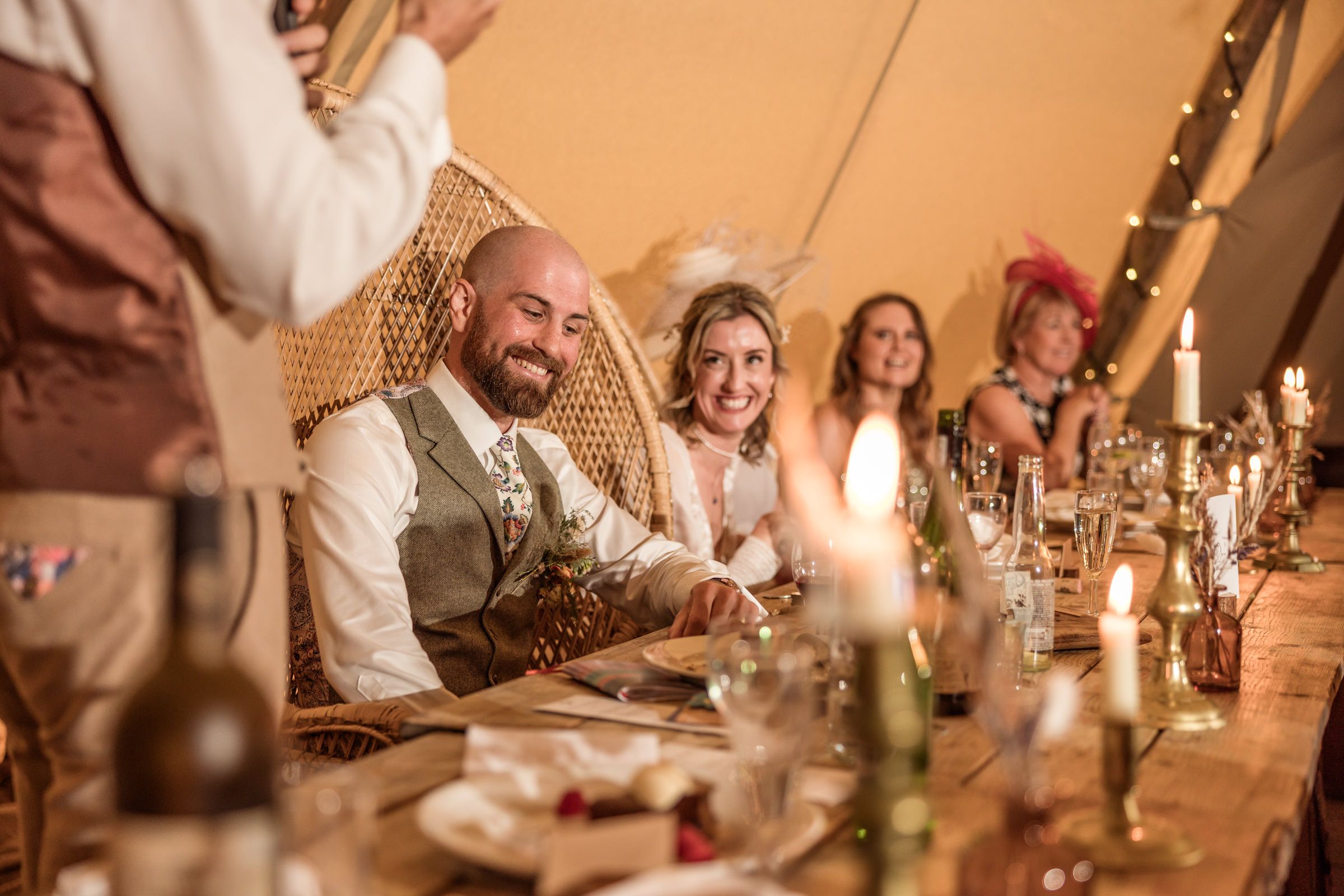 Wedding reception in a boho-style tent with wicker chairs and ambient lighting.