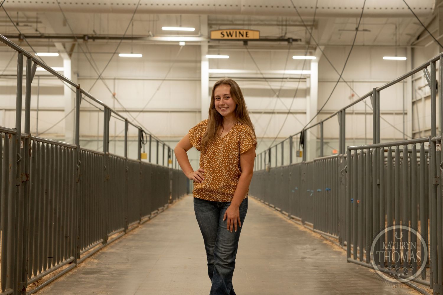 Standing portrait in swine facility hallway wearing spotted shirt and jeans.